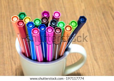 Many colorful pen in the cup on wooden background