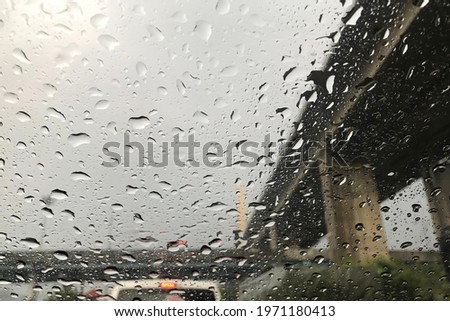 Rain drops on the windshield while the car is stuck in the city during the rain.