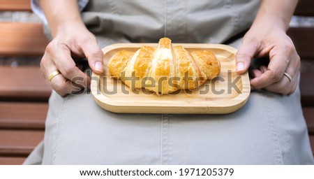 The woman's hand was picking up the croissant that had been placed on a wooden tray in her lap Royalty-Free Stock Photo #1971205379