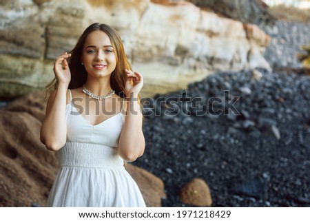 Gorgeous girl in a long white dress on the ocean at the beach. The model is inherited by nature. Girl on vacation, light dress, summer, fashion. Gorgeous long hair develops in the wind. Travel
