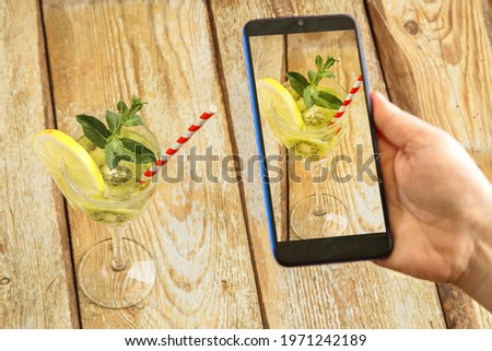 Cocktail with kiwi mint and lemon in a glass on a wooden table. Female hand takes pictures. Horizontal frame