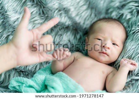 The newborn was wrapped in a green cloth, lying on a soft gray rug. She was acting innocent, holding her mother's little finger, and her mother made a symbol of hand, I love you.