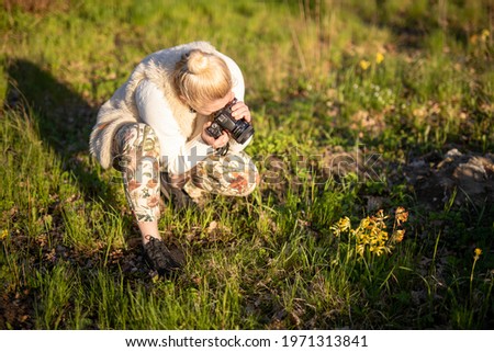 young woman photographs flowers in the meadow, spending free time, relaxing in the bosom of nature, amateur photography, nature photography