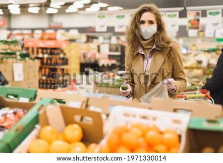 Shopping in a supermarket during pandemic. A woman in medical mask chooses the most necessary fruits and vegetables during covid-19 lockdown coronavirus. Restrictions to contain the spread the virus