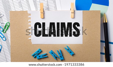 On the desktop are reports, blue clothespins and charts, a pen, a notebook and a sheet of paper with the text CLAIMS. Business concept