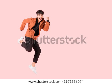 Happy handsome Asian man in fashionable clothing and jumping doing winner gesture isolated on pink background with clipping path. Portrait of young male cheerful jumping in air and smiling in studio. Royalty-Free Stock Photo #1971336074
