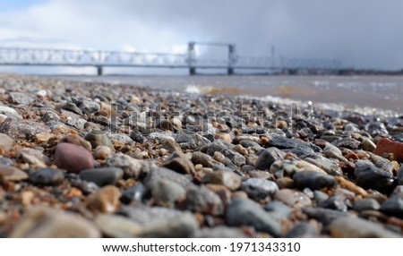 selective focus, pebble bank of the Northern Dvina river against the background of a large metal bridge and blue sky.