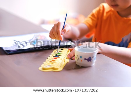 Close up of kids boy hands drawing , painting car cartoon pictures on wooden desk at home during covid-19 pandemic lockdown. Child fun art self learning, distance education and development background.