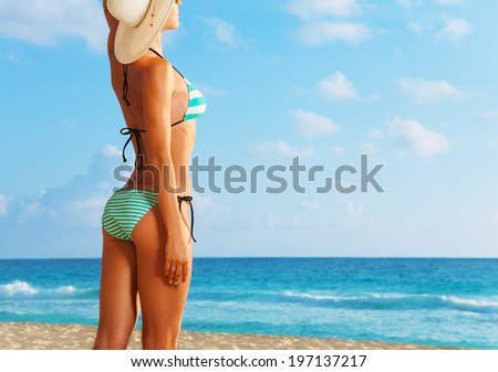 Close-up of young woman standing on the beach facing sun and looking at the ocean