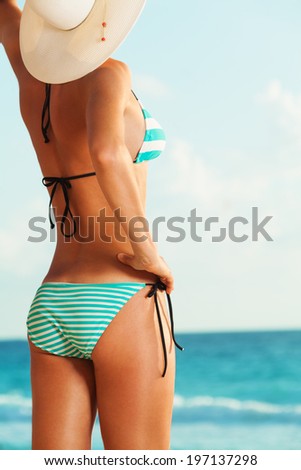 Beautiful body of the woman in bikini standing under the sun on the beach