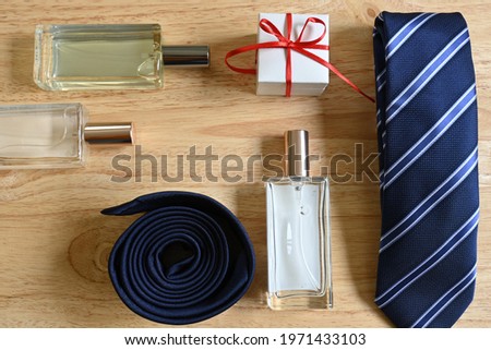 Flatlay of father's day gifts, square white gift box with red bow and tag with "happy father´s day" message, blue striped tie, three square perfumes, on pine wood background with copy space