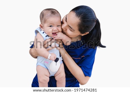 Happy child boy sucking fingers and looking at camera with a young woman kissing adorable baby boy isolated on white background. Pretty Asian female holding newborn baby grandson with love.