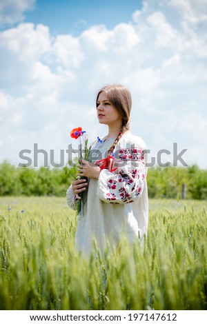 portrait of young woman cute Ukrainian blonde girl holding flowers in her hands standing in field happy smiling & looking into the distance at copy space on summer green outdoors blue sky background 