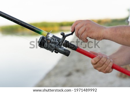 Fishing rod in male hands close-up. The guy fisherman twists the line and pulls the fish. River or estuary. Modern fishing tackle. Place for text