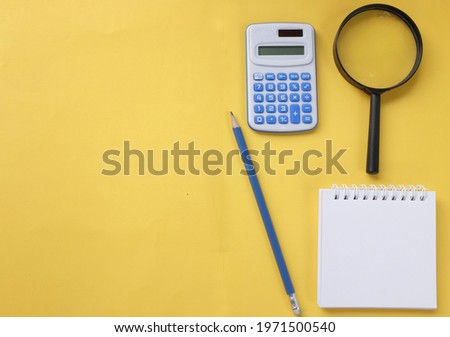  white spiral notepad ,pencil and magnifying glass ,blue Calculator isolate on a yellow background.concept Office or education equipment