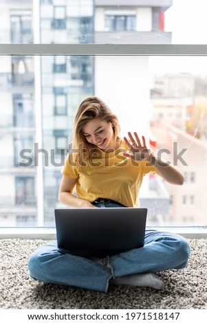Young woman having a videocall while sitting on a floor with laptop computer