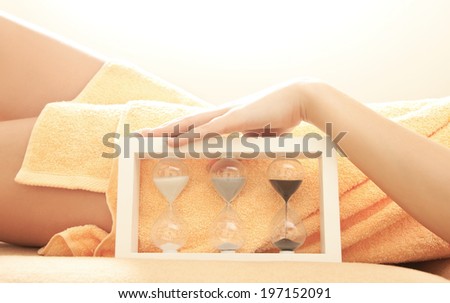 closeup picture of female hands and legs in spa salon with a sandglass