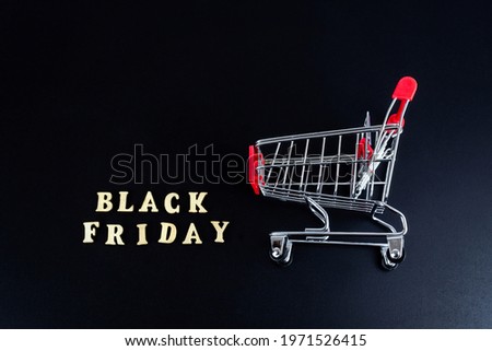 Black friday, discounts and season sales concept. Banner with grocery cart and words BLACK FRIDAY made from wooden letters on a black background. Top view, flat lay.