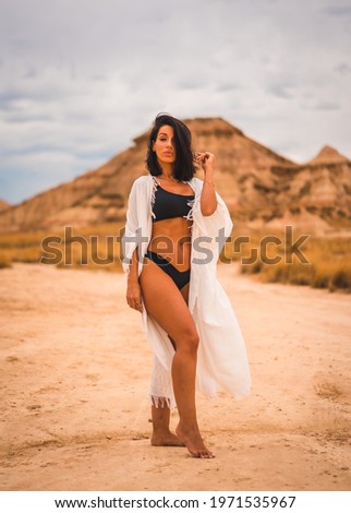 A young brunette Caucasian girl in a white dress and a black bikini posing in the desert