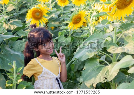 Asian cute little girl standing and smile in a pose with a finger while to travel the sunflower field.