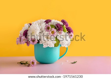 Summer bouquet of white chrysanthemum flowers in a blue cup on a yellow background. Summer flower background of chrysanthemum flowers. 