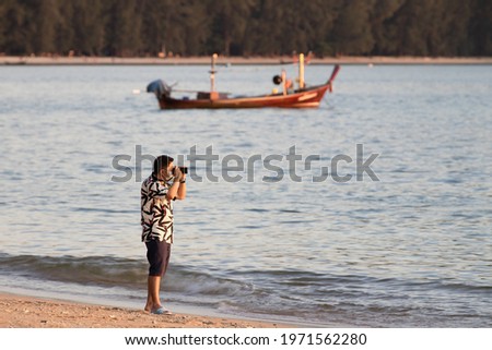 Male tourists taking pictures, on the beach, floating fishing boats.