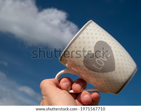A hand holds a mug in correspondence with a white cloud that seems to come out of the mug itself