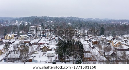 Winter rural landscape. Aerial view of a snow-covered village. Top view of the streets, houses and trees. Cold snowy winter weather. Snowfall. Snow on the roofs. Toksovo, Leningrad region, Russia. Royalty-Free Stock Photo #1971581168