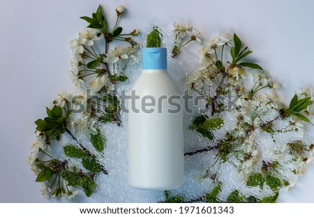 Trendy composition of plastic bottle with cosmetic and skin care products, flowering branches of spring trees and decorative glass. Natural organic cosmetic concept. Spa background with copy space.