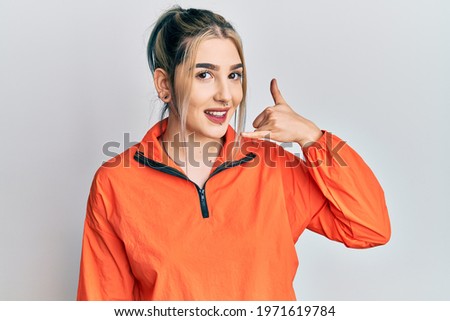 Young modern girl wearing sports sweatshirt smiling doing phone gesture with hand and fingers like talking on the telephone. communicating concepts. 