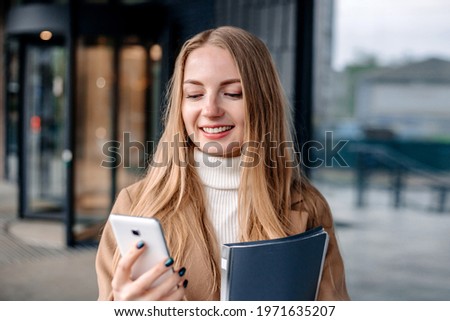 Young caucasian business woman looking at a mobile phone screen and smiling against the background of a dark office building