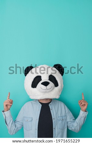 Funny man in panda mask man pointing up with hands to empty space. Copy space for text at the top