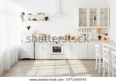 Kitchen with light walls, white furniture and shelves with crockery and plants in pots, small refrigerator in dining room scandinavian design, empty space. Modern interior with sunbeams on the floor