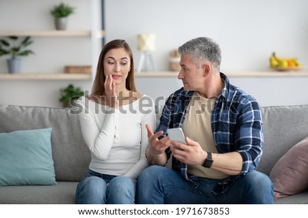 Mature man finding out about his wife's affair, confronting her about photos with lover on mobile phone. Middle-aged woman being accused of marriage infidelity, cheating on her boyfriend
