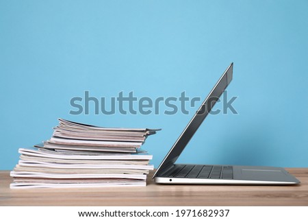 Laptop and stack of magazines on wooden table