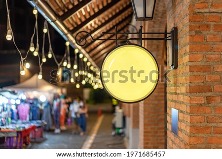 The Circle yellow Lightbox has hung on the wall in front of the brick pole in a Tungsten ambient environment vintage shopping community mall.