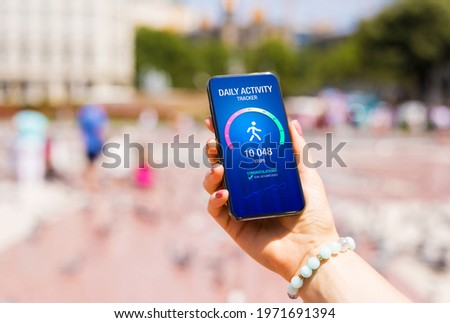 Woman using daily activity tracking app on phone showing 10 000 steps daily goal achievement Royalty-Free Stock Photo #1971691394