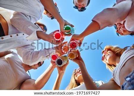 Low angle view of friends having fun at poolside summer party, clinking glasses with colorful summer cocktails near hotel swimming pool. People toast drinking fresh juice at luxury villa on vacation. Royalty-Free Stock Photo #1971697427
