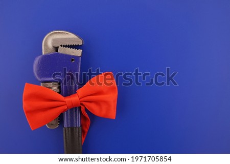 Pipe wrench tied with a red bow over a blue background with copy space. Labor Day or fathers day concept