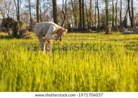young woman photographs flowers in the meadow, photographer leans over the plant
