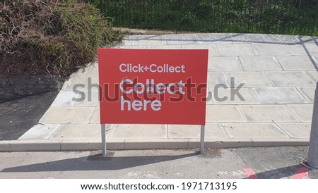 Red and white sign saying click and collect here in a car park. within a supermarket near Greater Manchester,  United Kingdom UK. with bushes and concrete  slab floor.