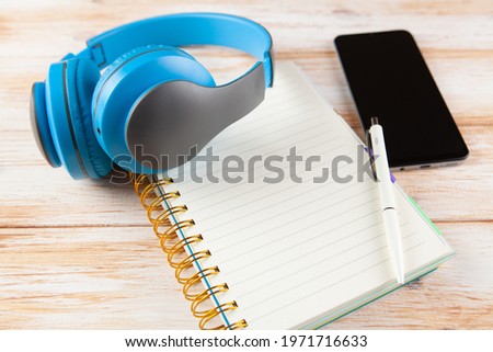 on a wooden background phone, notepad, pen and headphones