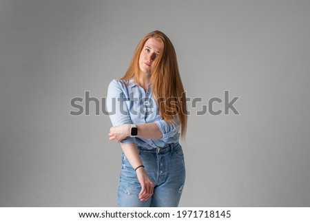 beautiful red-haired girl in a blue shirt and jeans in the studio against a white wall