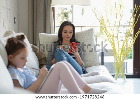 Happy mother smilling daughter sitting on sofa enjoying creative activity, drawing pen pictures in albums, mother and daughter spend free time together