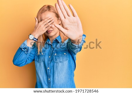 Beautiful caucasian woman wearing casual denim jacket covering eyes with hands and doing stop gesture with sad and fear expression. embarrassed and negative concept. 