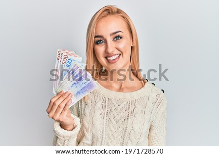 Beautiful caucasian woman holding swedish krona banknotes looking positive and happy standing and smiling with a confident smile showing teeth  Royalty-Free Stock Photo #1971728570