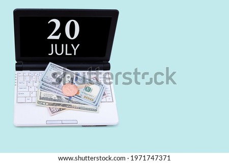 20th day of july. Laptop with the date of 20 july and cryptocurrency Bitcoin, dollars on a blue background. Buy or sell cryptocurrency. Stock market concept. Summer month, day of the year concept.