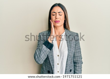 Young hispanic woman wearing business clothes touching mouth with hand with painful expression because of toothache or dental illness on teeth. dentist 