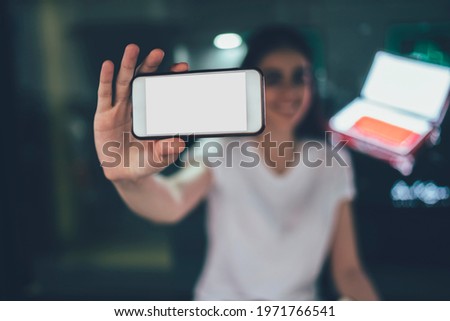 Blurred millennial user showing mockup smartphone gadget with copy space area during promotion photo session, female blogger shooting video vlog via camera on modern mobile gadget with blank screen