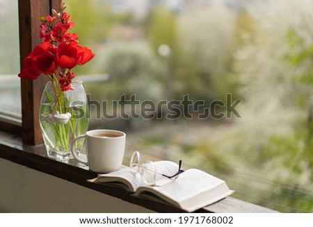 Book, glasses, cup of tea and red tulips on a wooden window. Read and rest. Cozy spring concept.